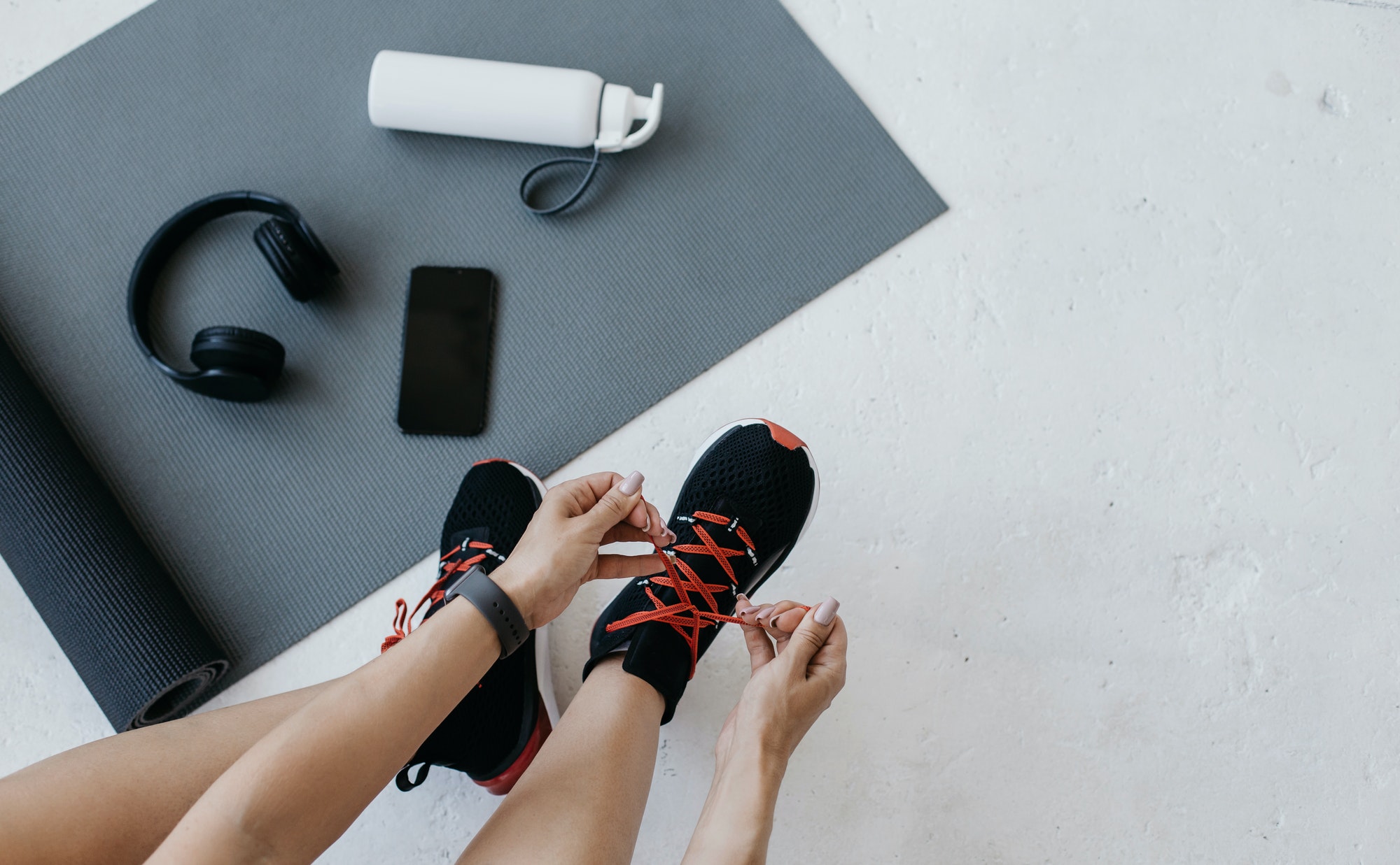 woman-athlete-with-fitness-tracker-ties-shoelaces-on-sneakers-sits-on-floor.jpg